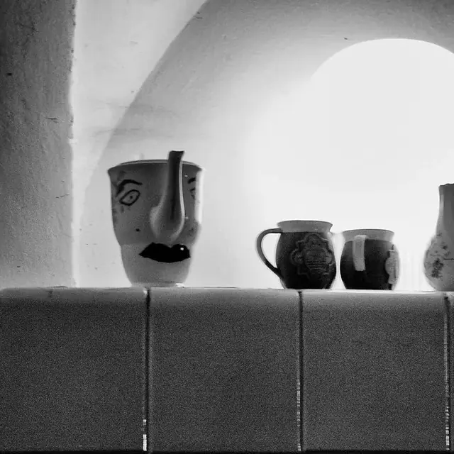 Dos jarras y dos tazas de cerámica sobre una repisa alicatada, bajo un arco encalado, en blanco y negro