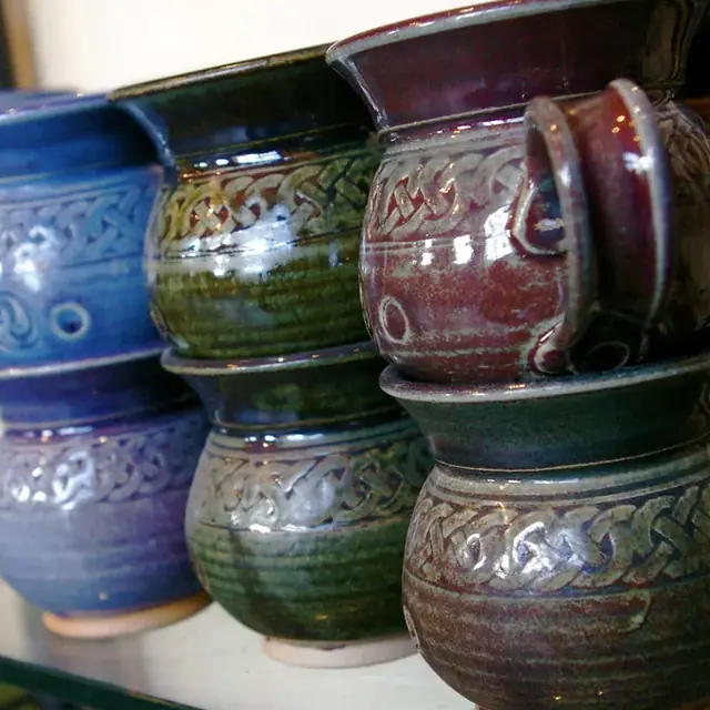 Tazas esmaltadas en azul, verde y granate, apiladas en una balda