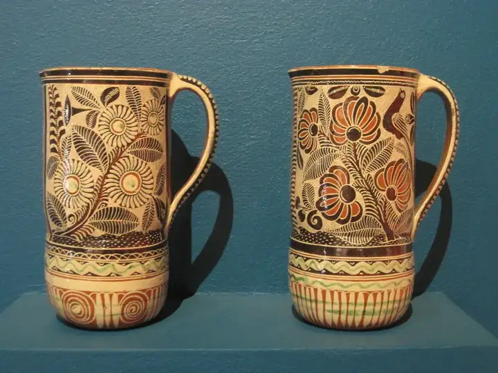 Dos tazas altas con asa tirada y decoración pintada bajo el esmalte, sobre un fondo azul