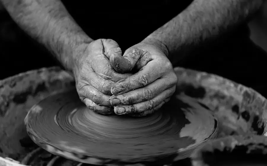 Dos manos ahuecadas sujetan el barro húmedo sobre el torno, en blanco y negro